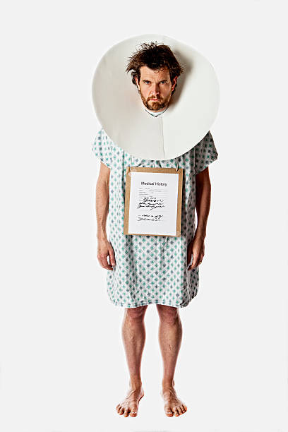 Unhappy looking man in hospital wear and a cone on his head stock photo