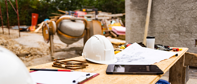 Architect blueprint, hardhat and work tools on wooden table while at construction site outdoors close up.