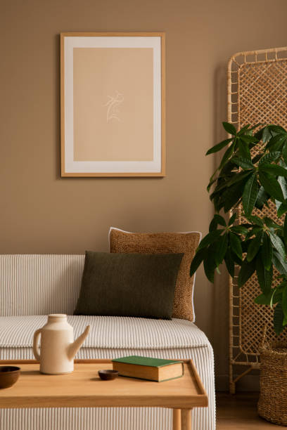 istock Creative composition of living room interior with mock up poster frame, beige modular sofa, brown pillows, book, plaid, partition wall, plant in basket and personal accessories. Home decor. Template. 1470737252