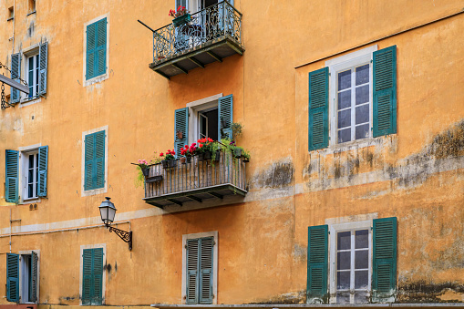 Facade of traditional mediterranean house with trompe l'oeil illusion painted on windows and flower pots on a balcony in the streets Old Town of Nice, France