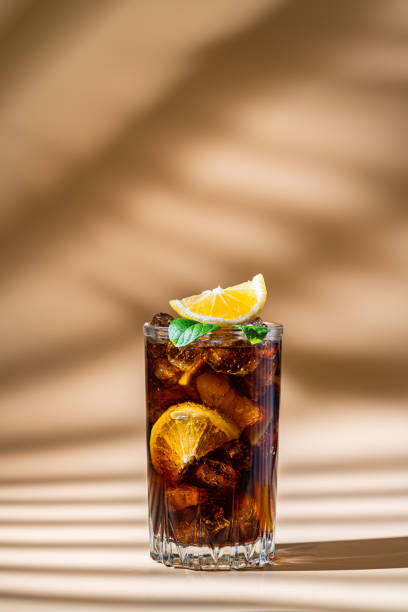Cuba Libre cocktail Cuba Libre in a glass with brown rum, cola, mint and lemon on light background with natural light and shadows. Cuba Libre or long island iced tea cocktail with strong drinks cuba libre stock pictures, royalty-free photos & images