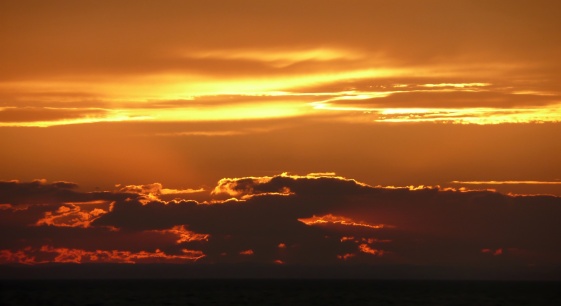 Heavenly orange and yellow sunset with gold lining over an ocean horizon.