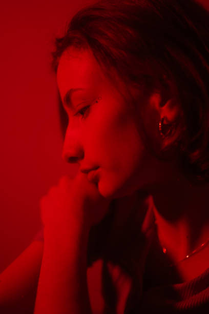 Young female model in a dark colorful lit studio environment posing against the wall and floor