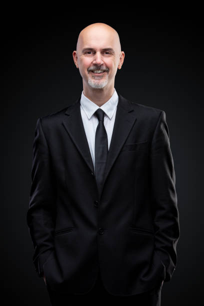 grey bearded businessman with hands in pocket looking at camera smiling friendly