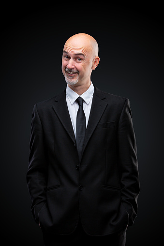 47 year old businessman looking at camera smiling questioning, black background