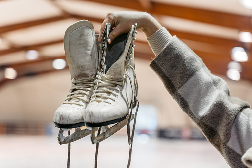 Close-up of a young woman holding up ice skates in the ice skating rink indoors.