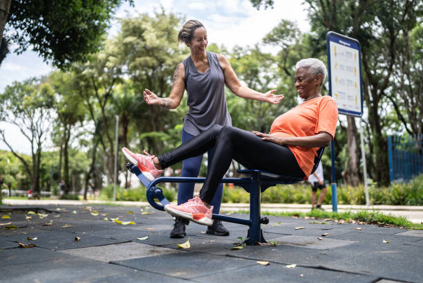 instructor de acondicionamiento físico dando instrucciones a una mujer mayor mientras hace ejercicio en el parque - gym machine smiling coach fotografías e imágenes de stock