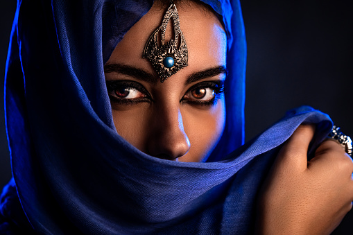 Portrait of a beautiful young woman wearing a blue hijab and jewelry.