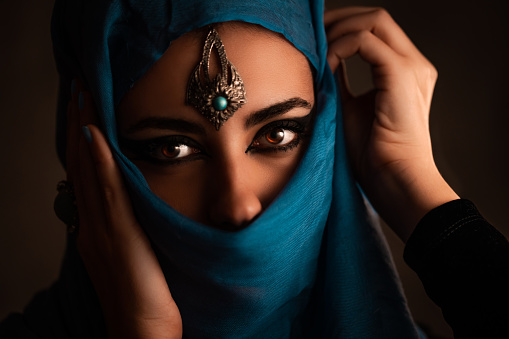 Portrait of a beautiful young woman wearing a blue hijab and jewelry.
