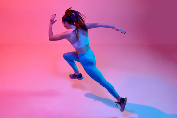 istock Top view dynamic image of professional female runner, athlete training over pink studio background in neon light. Concept of sport. health and strength 1470753494