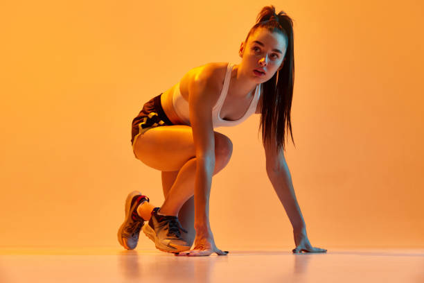 istock Ready to run. Young girl, professional female runner on start position, training over orange studio background in neon light. Concept of sport. health and strength 1470753610