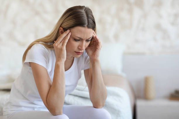istock Unhappy young lady sitting on bed, rubbing her temples 1470755136