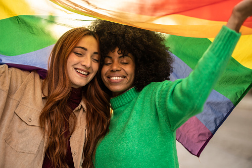 Two loving women with pride flag - multiracial lesbians millennial generation,