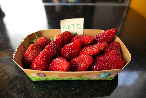 Some delicious, real organic strawberries in a paper container on a black surface with an adhesive note label with the text 