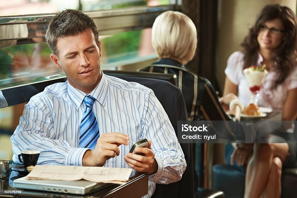 Businessman using mobile in cafe Businessman sitting at table in cafe using mobile phone. Young women having sweets in the background. 30-39 Years Stock Photo