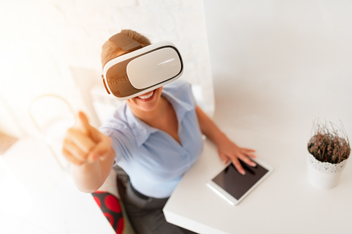 Happy businesswoman using virtual reality glasses in a cafe.