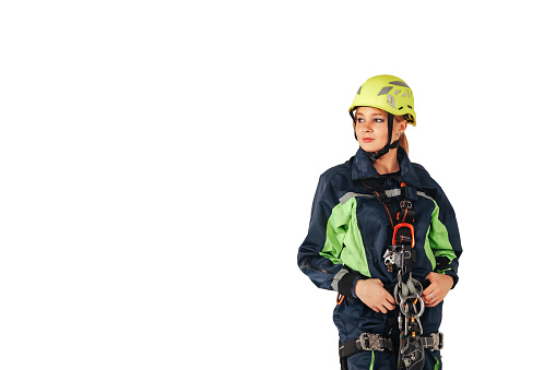 Industrial young woman in industry uniform and protective helmet posing at isolated white empty background, looking away. Serious female worker in workwear standing in isolation. Copy text space