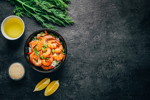 top view of a dish of rice and shrimp in a plate next to sauce herbs and butter on a dark background with free space for text