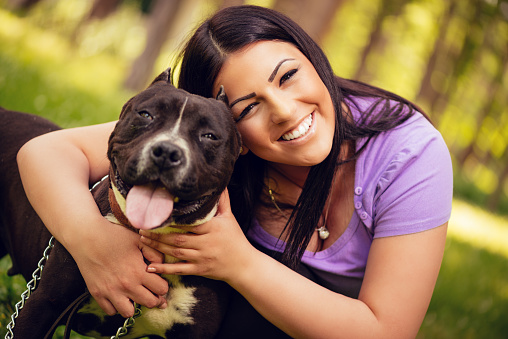 Portrait of a beautiful young woman hugging her cute stafford terrier in the park and enjoying. Looking at cemera.