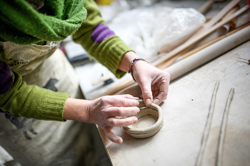 Close up of female hands working with clay making a cup in a workshop. Selective focus.