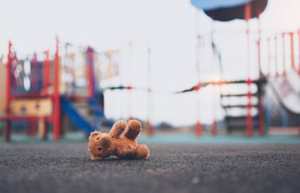 Lost teddy bear toy lying don on playground floor in gloomy day,Lonely and sad brown bear doll lied down alone in the park,lost toy or Loneliness concept,International missing Children day juguete de oso de peluche perdido acostado don en el piso del patio de recreo en un día sombrío, muñeca de oso pardo solitaria y triste acostada sola en el parque, juguete perdido o concepto de soledad, día internacional de los niños desaparecidos