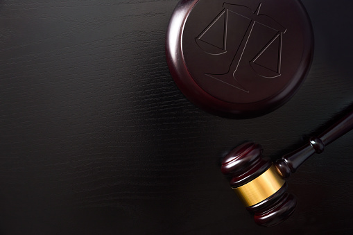 Background with symbolic objects of justice such as gavel and balance on black wooden table. Top view