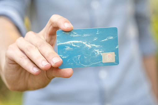 Man holding a blue premium VIP social club membership advantage card in hand, empty template, mockup, clouds, copy space, card object closeup, one person. Credit card, debit card, banking, discounts