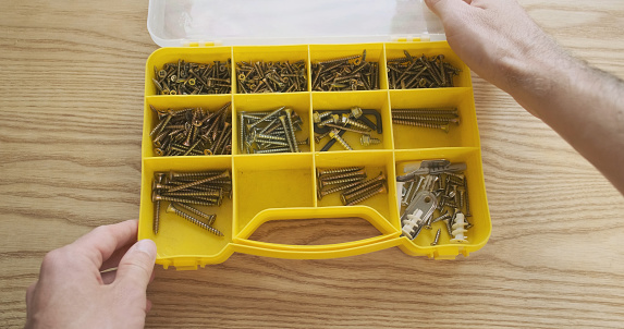 Man's hand opens a plastic box with screws. Selects the desired screw. First-person view, close-up. High quality photo