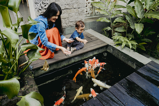 Pretty mother and a young baby relax on a rock while watching the Koi fish swim by