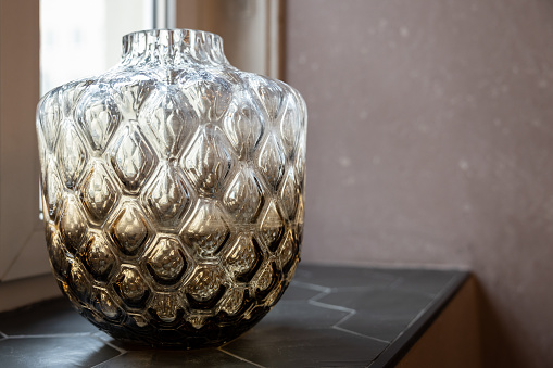A three-dimensional glass vase with a relief pattern stands on a dark granite window sill. High quality photo