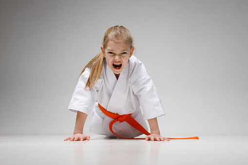 A strong little girl in a kimono does push-ups from the floor at a karate training.