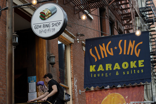 New York, NY, USA - July 5, 2022: Young people enter the building that houses the Gem Bing Shop and Sing Sing Karaoke Lounge & Suites in the East Village neighborhood in Manhattan, New York City.