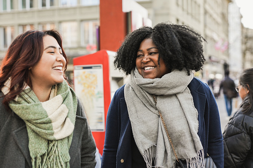 Young multiracial women having fun together waiting at the tram station during winter time