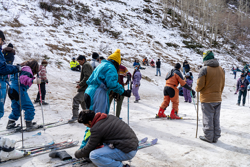 Kullu, India - circa 2022: Panning shot of crowd of people in winter wear playing in snow, sking, sliding, at snow point in lahul, manali solang a popular tourist spot during winters