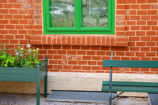 Cottage with brick wall, green windows, bench and colorful flowers.