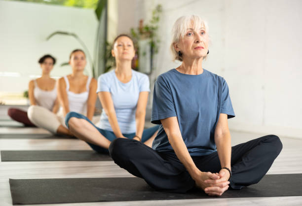 istock Old female gym visitor practicing Butterfly Pose Baddha Konasana during group yoga training 1470783565