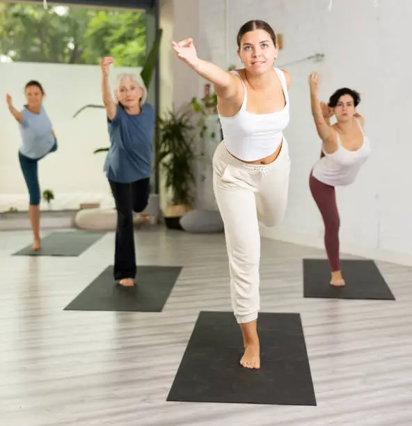 Photo of Young girl and group of active females performing yoga in fitness studio
