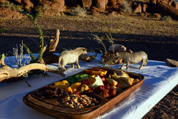 Various snacks on a wooden tray: nuts, buns, fruit in the fresh air with decorations in the form of zebra figurines