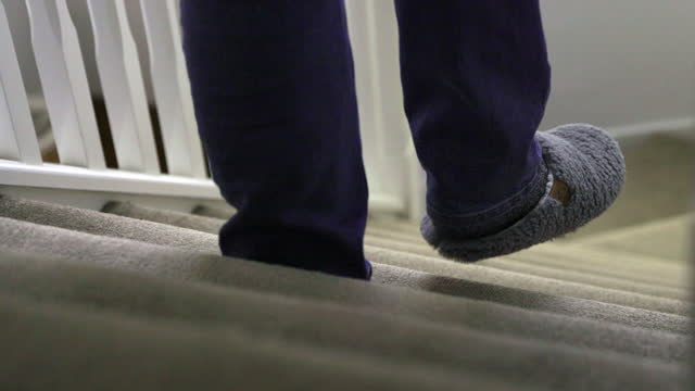 Walking downstairs indoors wearing slippers, shot from top of stairs. Lower body, feet and legs.