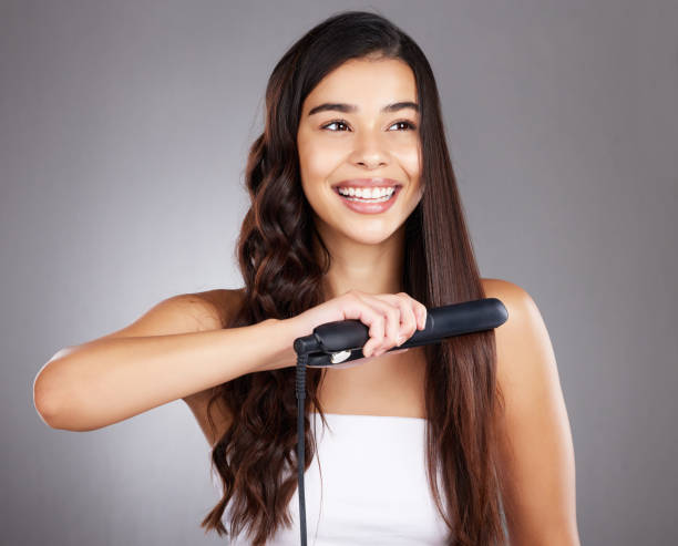 Hair care woman, studio and flat iron with smile, focus and happy for self care cosmetics by backdrop. Model, hair and self love with happiness, aesthetic and product for beauty, wellness and health cuidado del cabello mujer, estudio y planchita con sonrisa, feliz para los cosméticos de cuidado personal por telón de fondo. modelo, peluquería y salón con felicidad, estética y producto para la belleza, el bienestar, el brillo o la salud