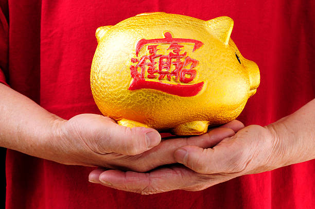 Typical Chinese Business Piggy Bank Held By Hands, with traditional Chinese characters on the Piggy Bank's side saying \