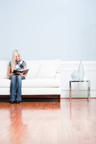 istock Young Woman Sitting on Sofa Reading Book 147078923