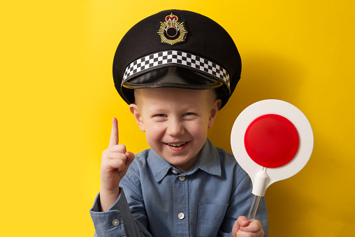 Boy in a cap of a policeman showing index finger up at a red traffic light on a yellow background