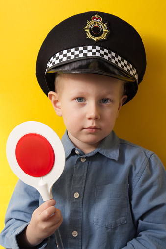 Boy in a cap of a policeman showing a red traffic light on a yellow background