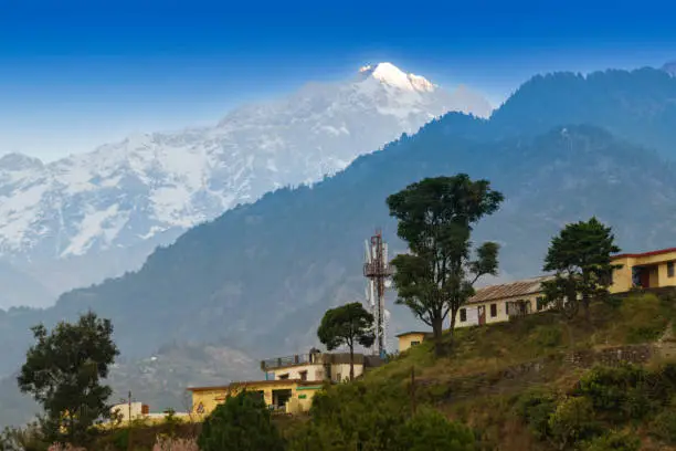 Photo of Snow capped mountain peak of Choukhamba range with tourist bungalows and resorts at Deoriatal, Uttarakhand, India. Sun set light on peak of famous Garhwal Himalayan mountain range.