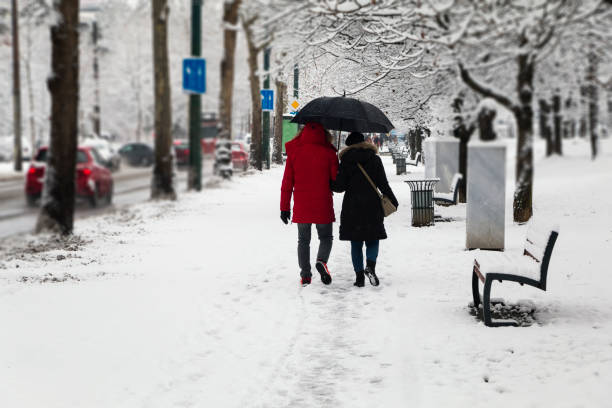 Senior adult couple walking on snowing sidewalk. Winter landscape.