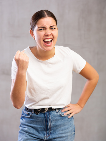 Portrait of aggressive young woman standing in threatening position against light unicoloured background