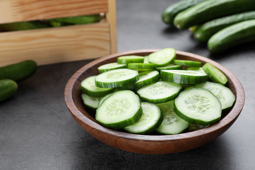 Slices of fresh ripe cucumber in bowl on grey table, closeup