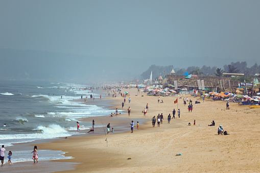 Feb 26, 2023 - Candolim Goa India: Sunny morning view of the Goa beach filled with tourists. All the beach side restaurants are open and people are enjoying the sea.