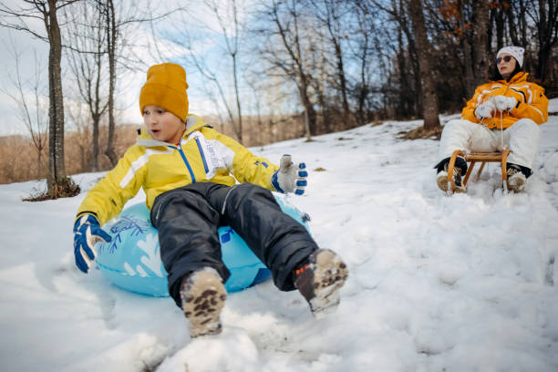 Boy having fun on snowy mountain sledding together with his mother